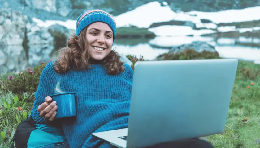 Kvinna med mugg och laptop i fjällen, studerar konstvetenskap distans.