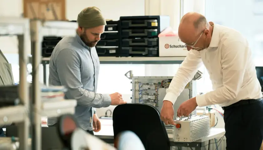 Två män arbetar med elektronik. En creative director ser på när en kollega kopplar ihop komponenter.