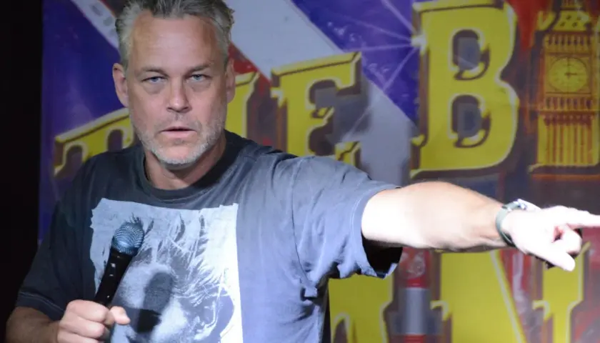 En stand up komiker i Sverige pekar med ena handen och håller en mikrofon i den andra.