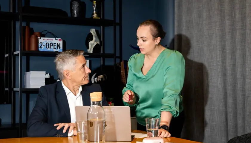 En kvinna i grön blus diskuterar med en man i kostym vid ett bord. De verkar ha ett möte, kanske som hr partner.