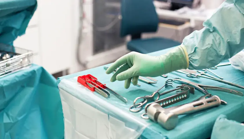 Steriltekniker utbildning: En hand i grön handske plockar bland sterila kirurgiska instrument på ett operationsbord.