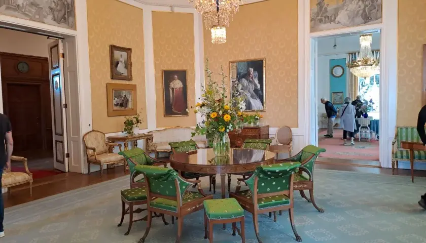 Elegant room with a round table, green chairs, floral arrangement, and paintings on yellow walls.