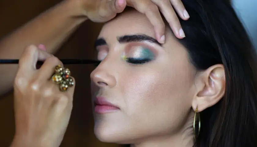 En makeupartist utför en professionell utbildning. En kvinna får en grön och silverfärgad ögonsminkning.