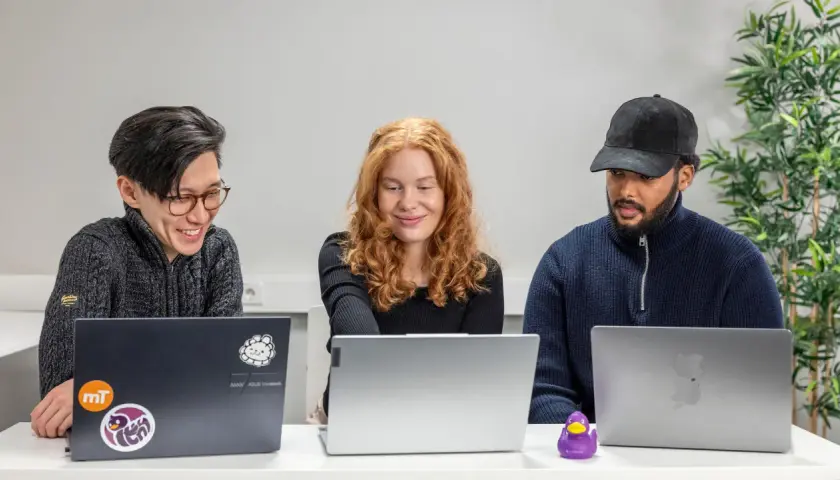 Tre personer arbetar vid sina laptops. En data scientist med rött hår ler.