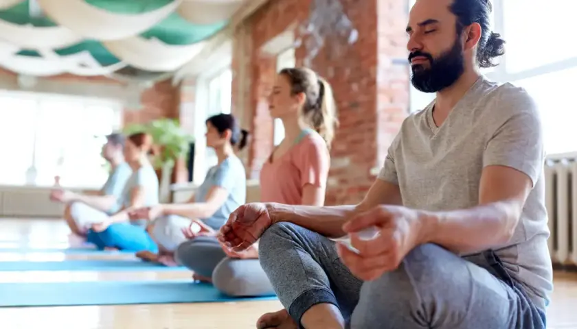 Människor med slutna ögon sitter i lotusställning på yogamattor. En grupp som deltar i en yoga utbildning distans.