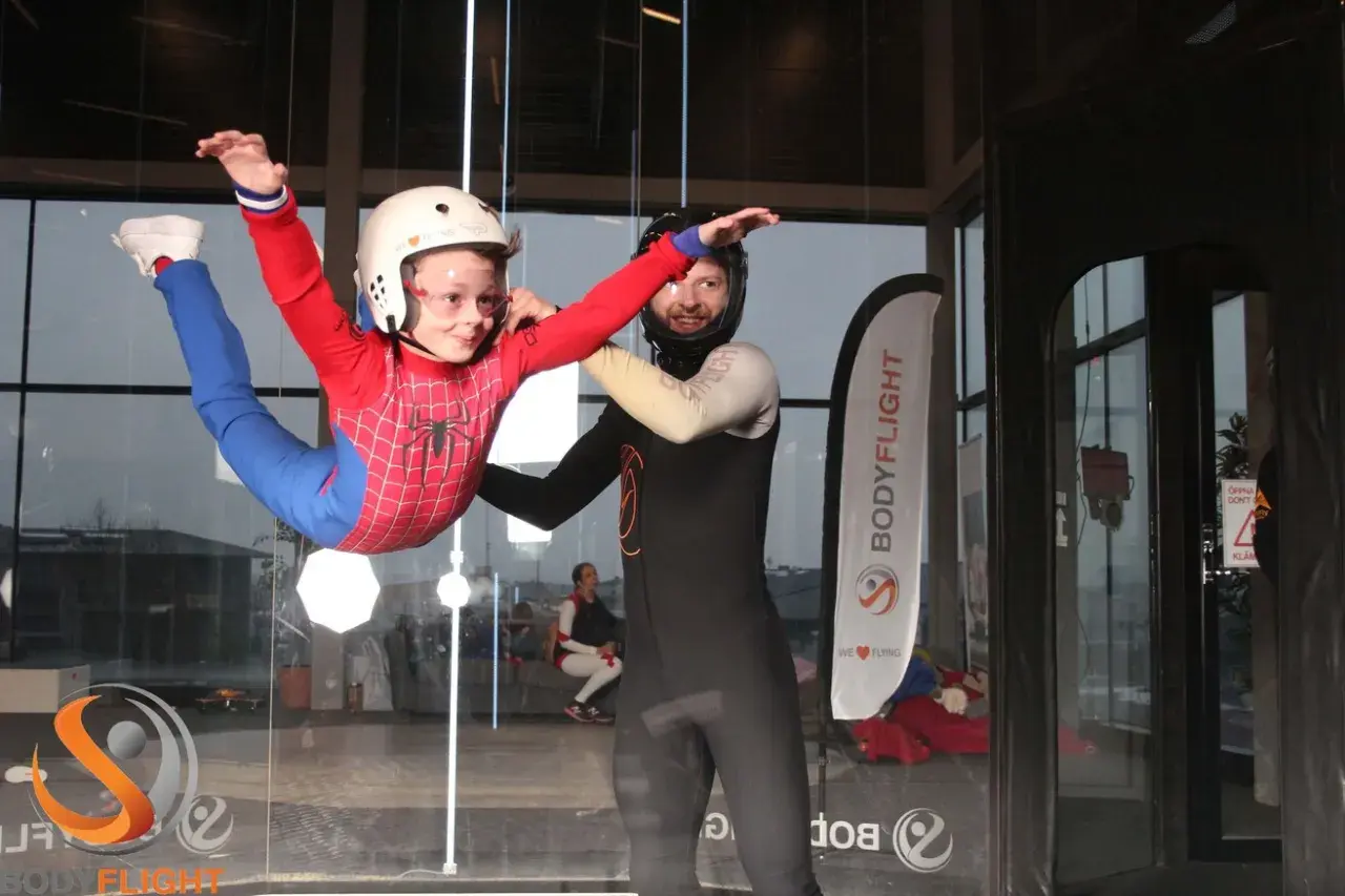 Barn i Spindelmannen-dräkt flyger i vindtunnel, en av många roliga aktiviteter i Stockholm. En instruktör hjälper till.