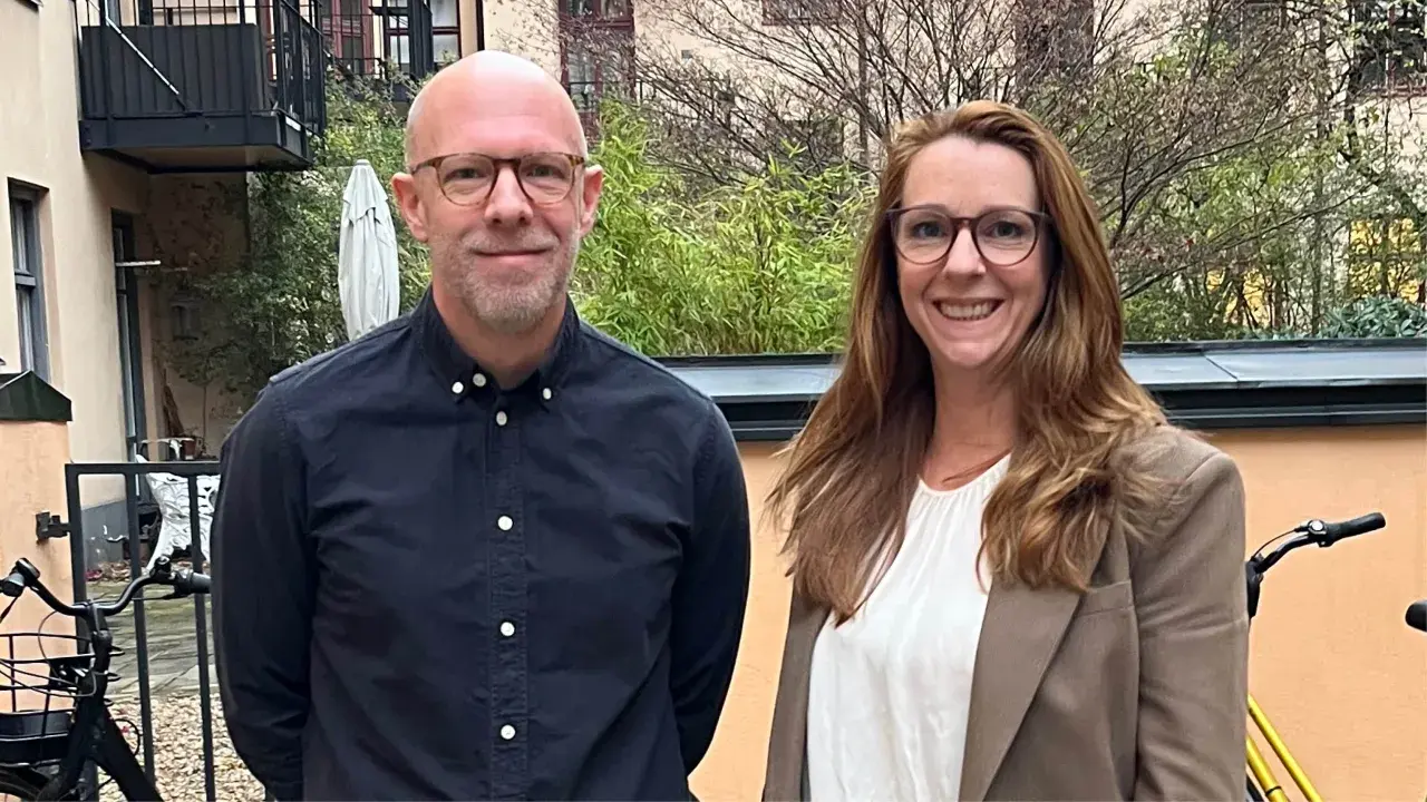 Två leende personer, en man och en kvinna, står utomhus. Kanske är de kollegor som diskuterar vinnova lediga jobb.