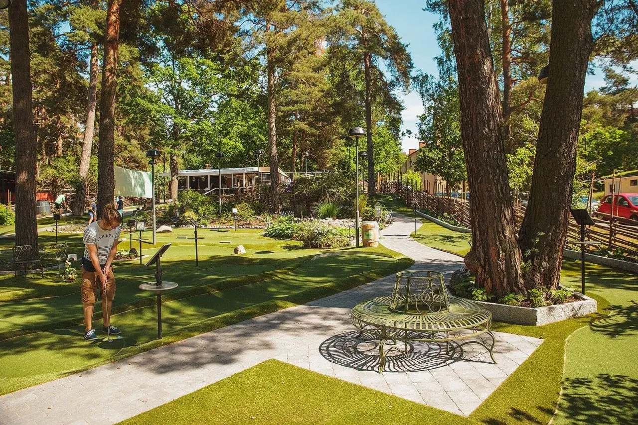 En person spelar minigolf i Aspudden, omgiven av grönska och träd. En vacker sommardag för en runda minigolf.