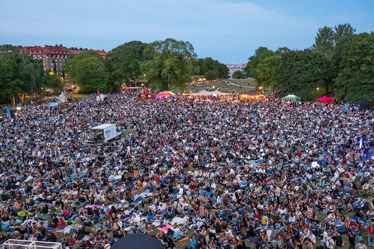 Stor publik samlad för utomhusbio i Stockholm. Tusentals människor sitter på filtar i en park och tittar mot en scen.
