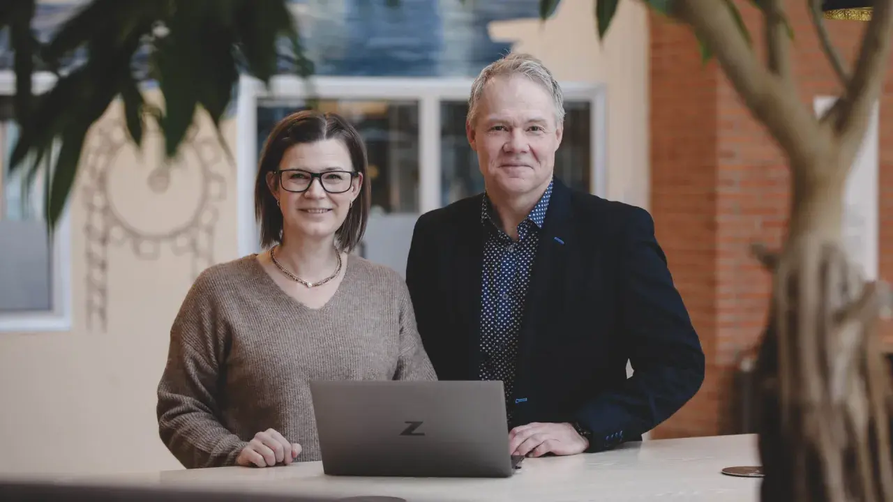Två kollegor ler vid en laptop. De är på ett kontor i Stockholm, kanske för en praktik.