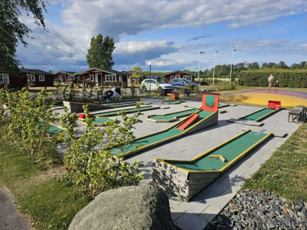 En minigolfbana vid Slottsskogen med röda stugor i bakgrunden. En ko-staty står vid en bana.