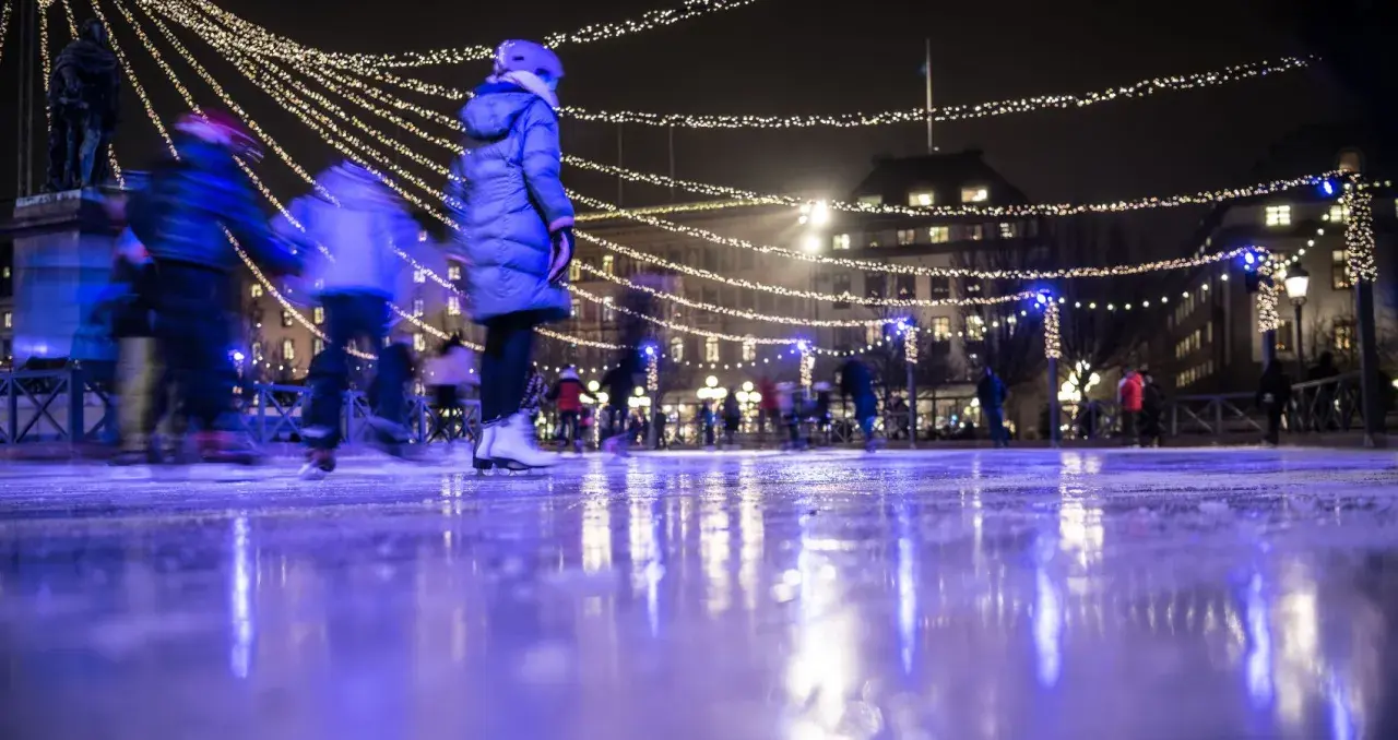 Människor njuter av kungsträdgården ice skating under gnistrande ljus. Isen reflekterar den magiska stämningen.