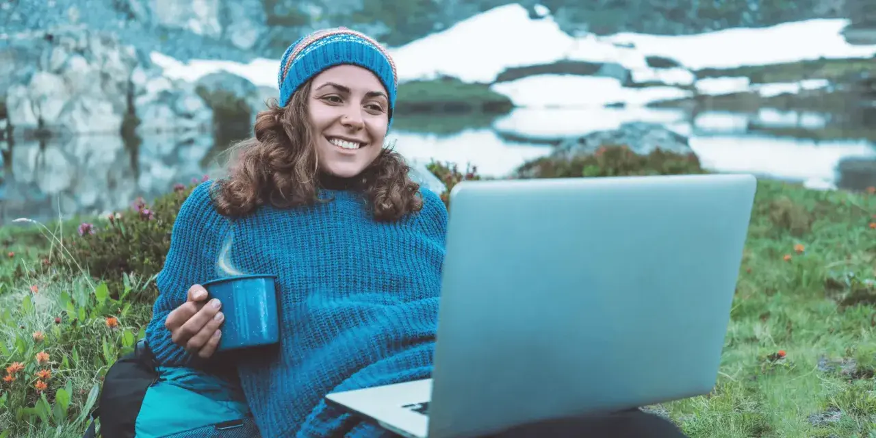 Kvinna med mugg och laptop i fjällen, studerar konstvetenskap distans.