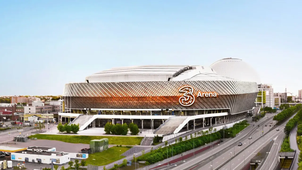 En stor arena med "3 Arena" logotypen. Området runt arenan är fullt av globen aktiviteter, med vägar och byggnader.