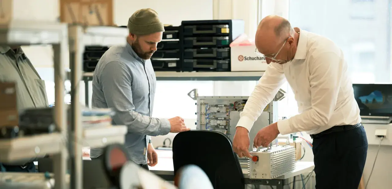 Två män arbetar med elektronik. En creative director ser på när en kollega kopplar ihop komponenter.