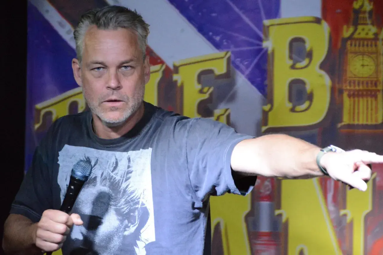 En stand up komiker i Sverige pekar med ena handen och håller en mikrofon i den andra.