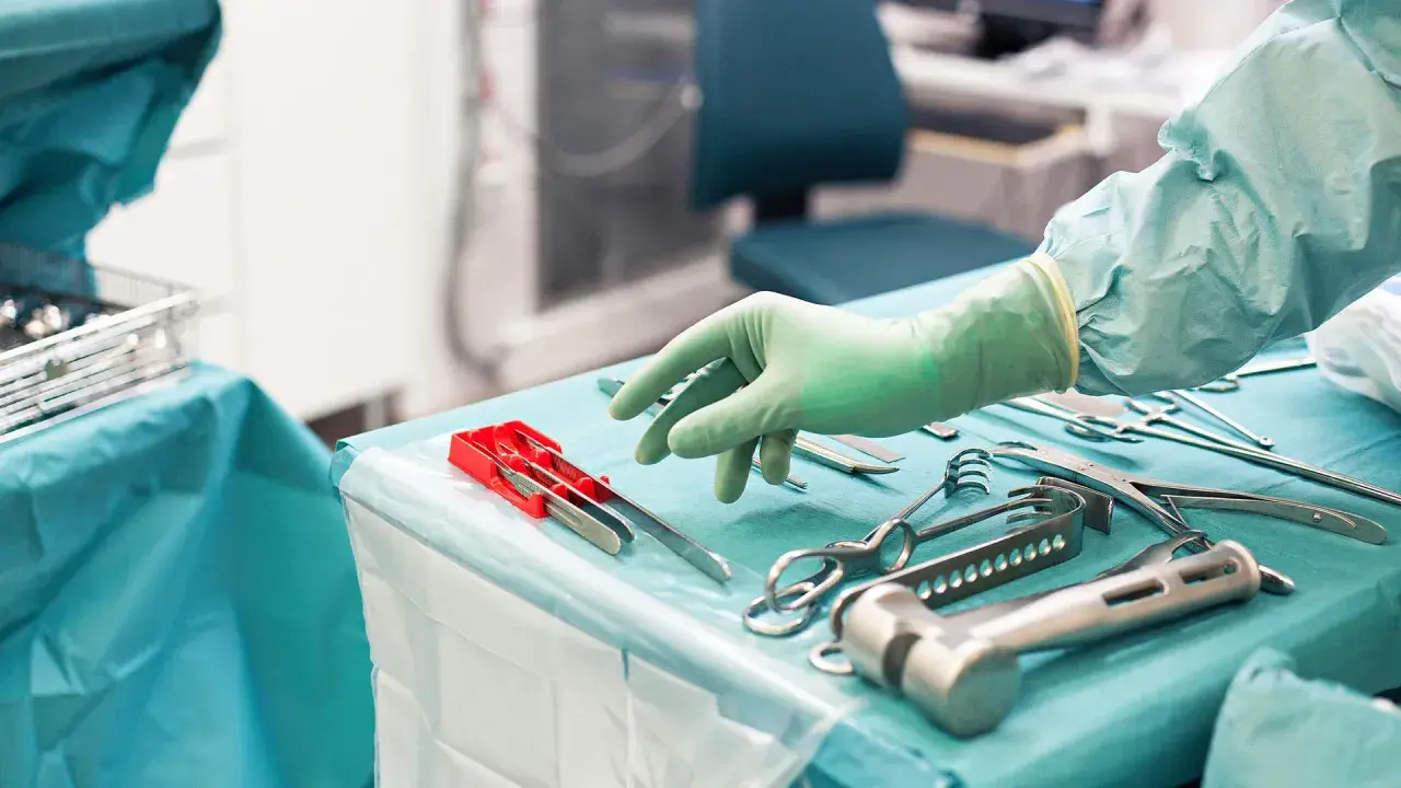 Steriltekniker utbildning: En hand i grön handske plockar bland sterila kirurgiska instrument på ett operationsbord.
