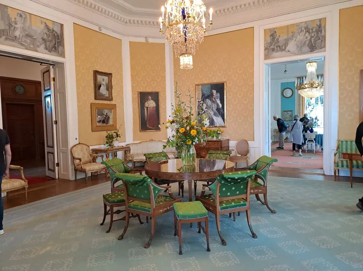 Elegant room with a round table, green chairs, floral arrangement, and paintings on yellow walls.