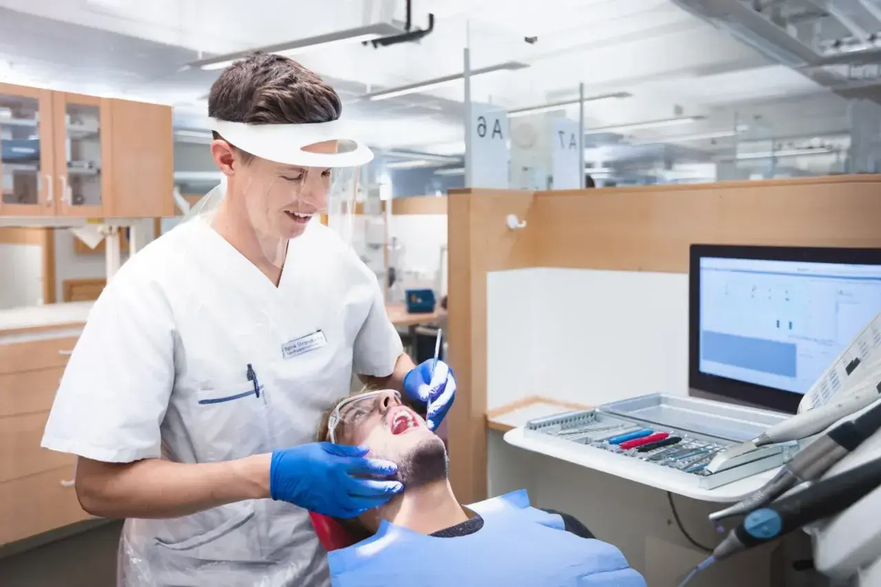 En tandhygienist i skyddsutrustning utför en undersökning på en patient. Detta är en del av en tandhygienist utbildning.