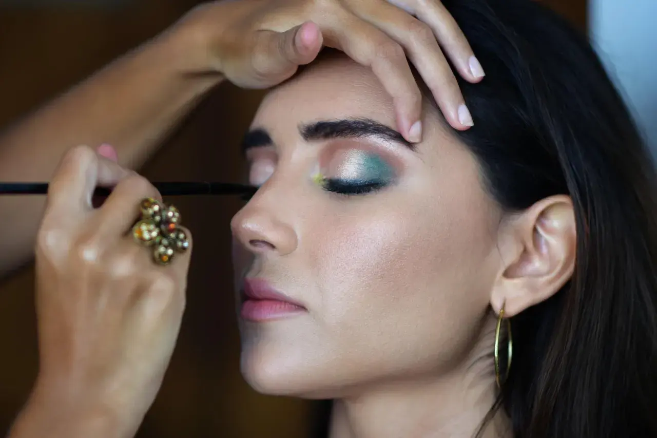 En makeupartist utför en professionell utbildning. En kvinna får en grön och silverfärgad ögonsminkning.