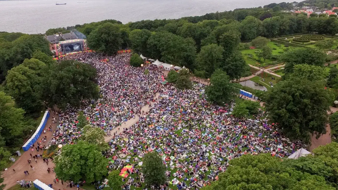 Stor publik njuter av en konsert i botaniska tr&auml;dg&aring;rden. M&auml;nniskor sitter p&aring; filtar p&aring; gr&auml;smattan framf&ouml;r en scen.