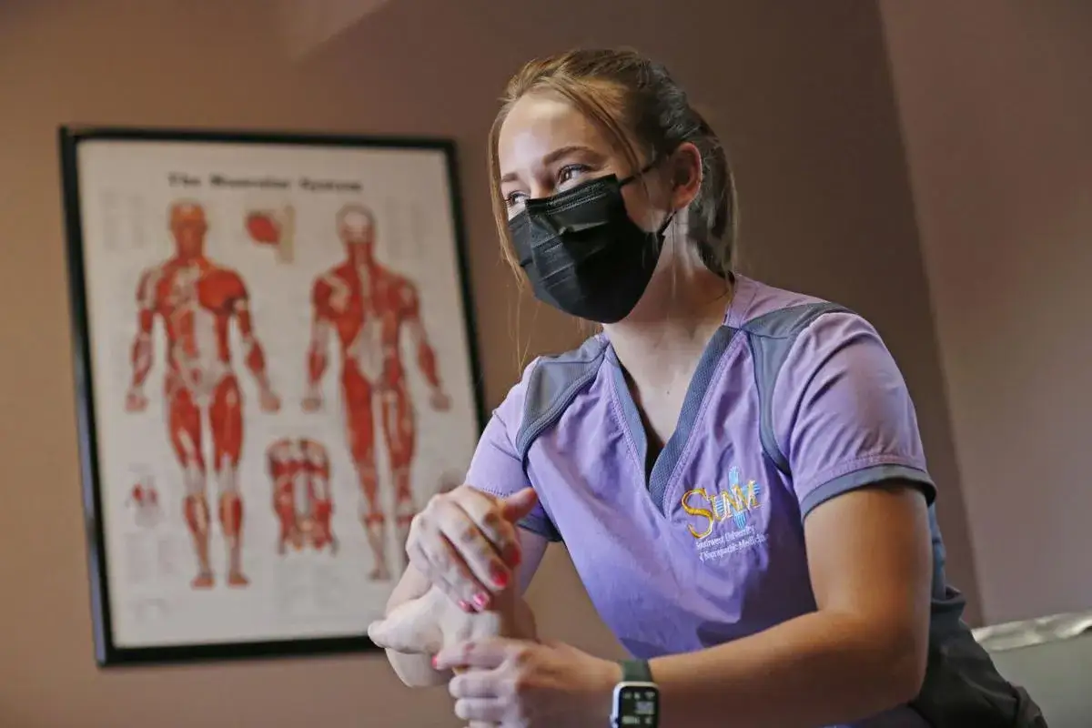 En student på naprapatutbildning utför en fotbehandling. I bakgrunden syns en anatomisk plansch över muskelsystemet.
