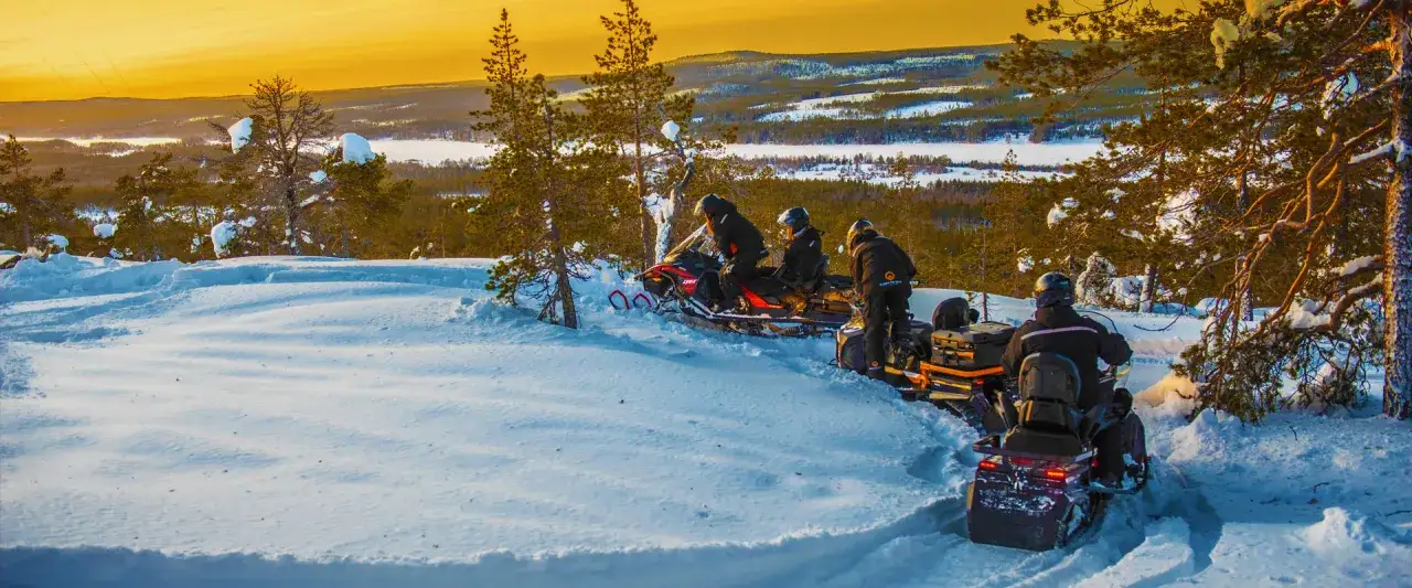 Sn&ouml;skoter&aring;kare njuter av vinterlandskapet i Norrbotten. Solnedg&aring;ngen f&auml;rgar himlen gyllene &ouml;ver sn&ouml;t&auml;ckta tr&auml;d och fj&auml;rran sj&ouml;ar. Perfekta aktiviteter Norrbotten f&ouml;r &auml;ventyrare.