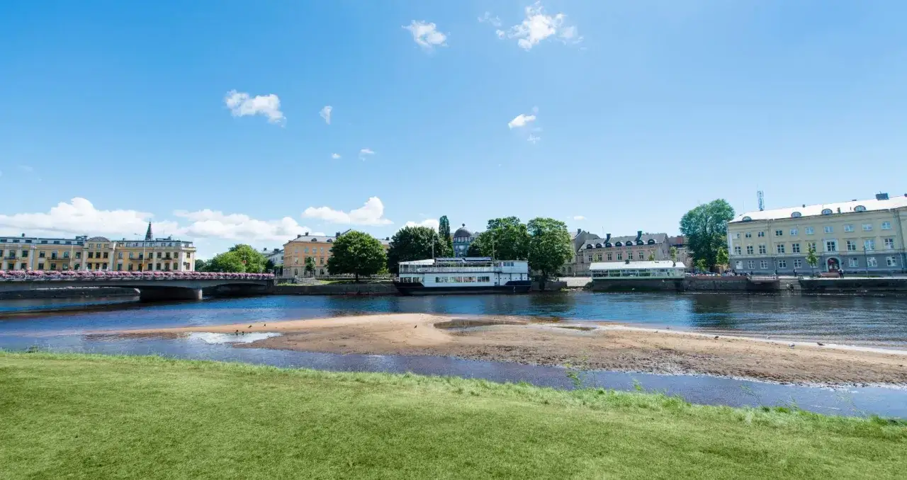 En solig dag vid Klarälven i Karlstad. En bro med blommor, en båt och vackra byggnader. Perfekt för gratis aktiviteter Karlstad!