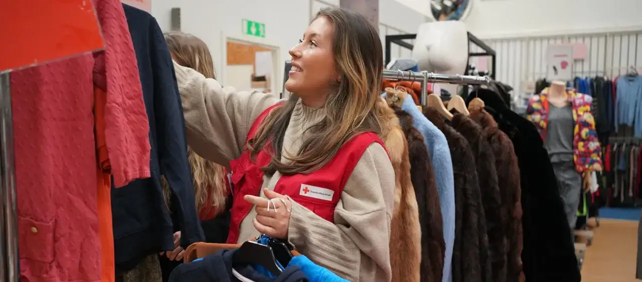 En kvinna i r&ouml;d v&auml;st fr&aring;n R&ouml;da Korset sorterar kl&auml;der i en butik. Kanske hon letar efter myrorna lediga jobb h&auml;r?