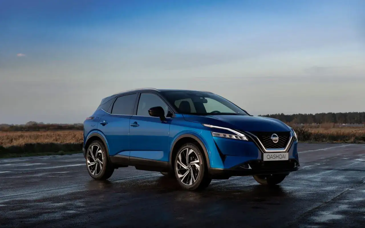 Blå Nissan Qashqai parkerad på en våt vägbana. Undrar du hur mycket kostar det att leasa en bil?