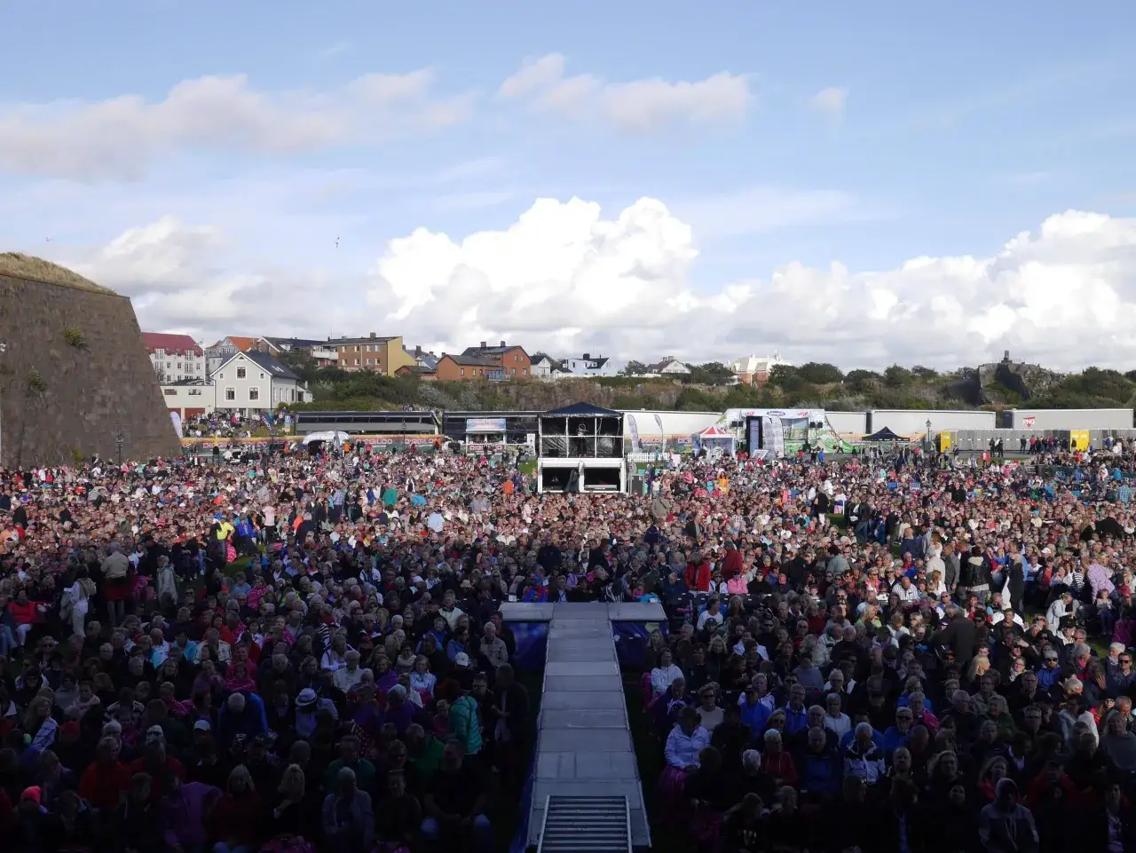 Stor publik samlad för Diggiloo i Varberg. En solig dag med moln på himlen, folk sitter på gräset och njuter av evenemanget.