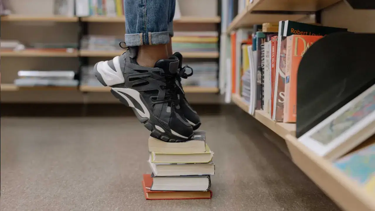 En person står på böcker i ett bibliotek. Kanske är det ett steg på vägen för att lära sig hur blir man bibliotekarie.