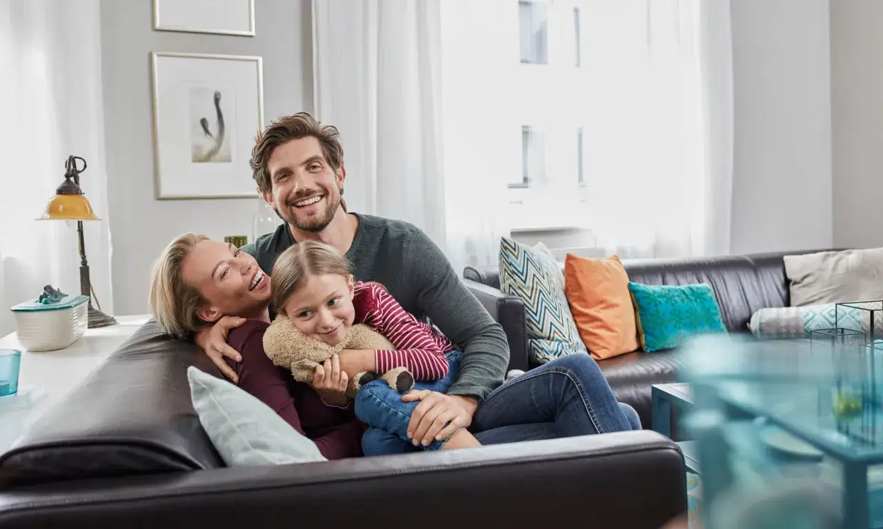 En glad familj myser i soffan. Pappan funderar på hur mycket ska man spara till pensionen för att kunna njuta av framtiden.