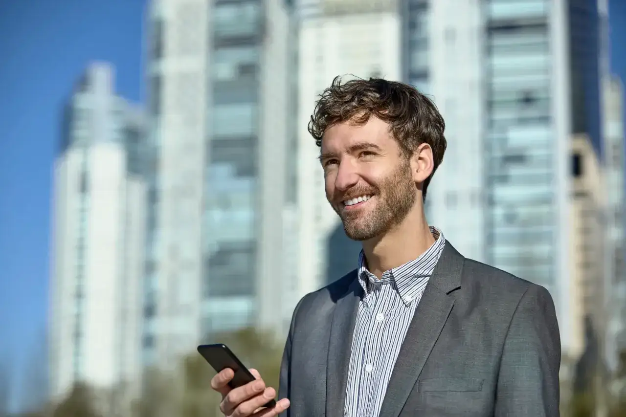 Man med mobiltelefon framf&ouml;r skyskrapor. Han ler och verkar n&ouml;jd med sin utbildning inom fastighet.