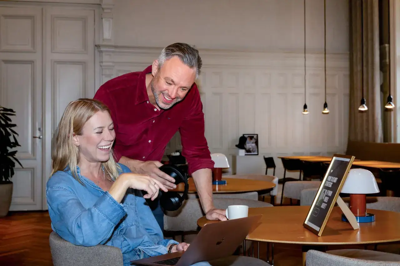 Två kollegor, en front end utvecklare och en man, skrattar vid en laptop i ett modernt kontorslandskap.