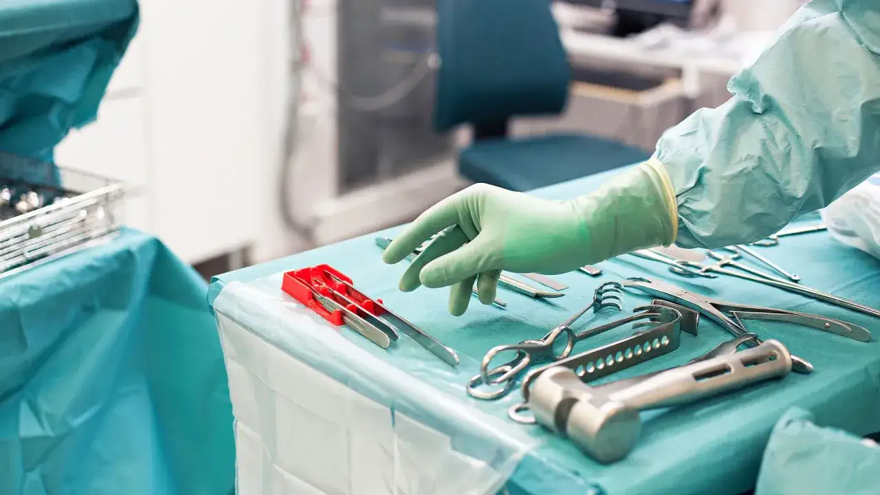 Steriltekniker utbildning: En hand i grön handske plockar bland sterila instrument på ett operationsbord.