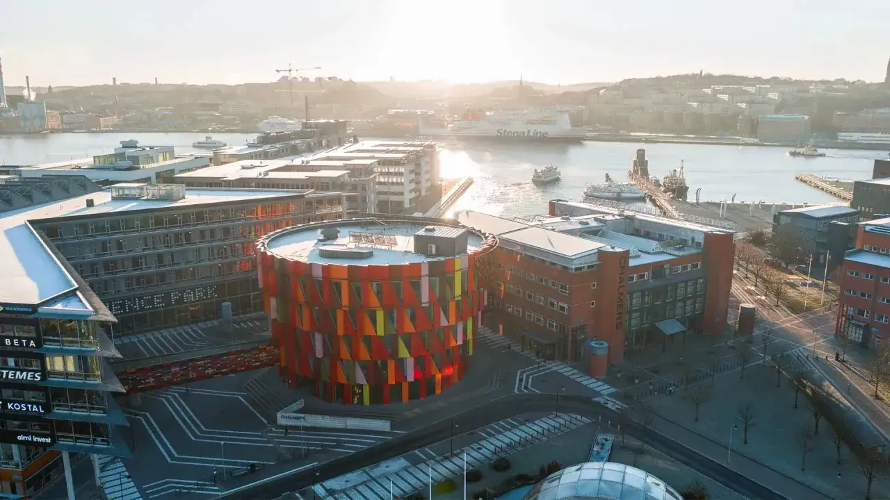 Solnedgång över Lindholmen Science Park, Göteborg. Byggnader med modern arkitektur och en färgglad, rund byggnad. I bakgrunden syns hamnen med fartyg, inklusive Stena Line. Här bedrivs forskning inom bland annat internationell logistik vid Chalmers.