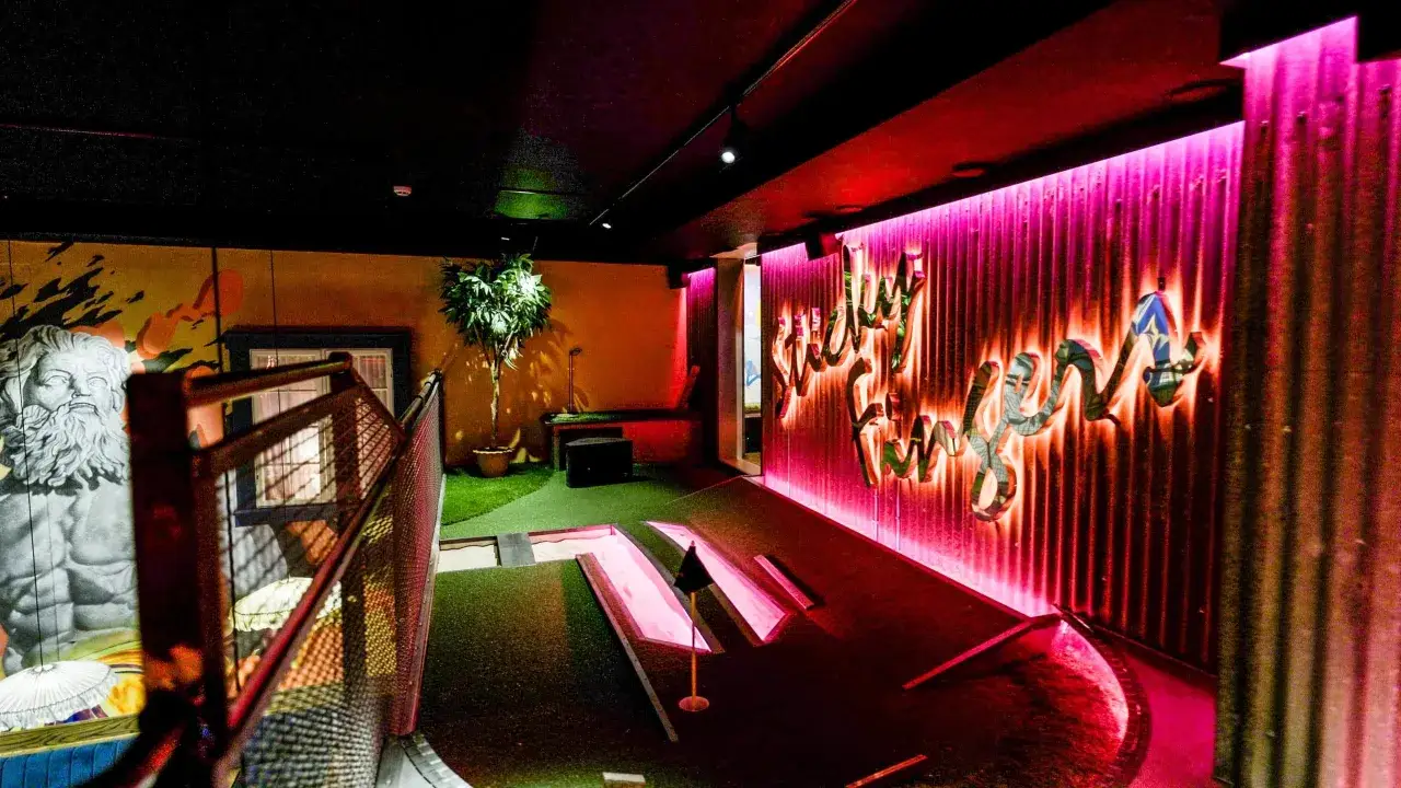 En neonupplyst minigolf bar med en väggmålning av en grekisk gud och en korrugerad vägg med texten