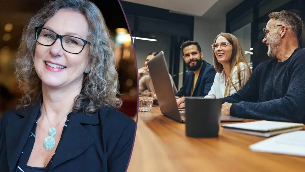 En leende kvinna med glasögon, troligen en hr chef, deltar i ett möte med kollegor vid ett konferensbord.