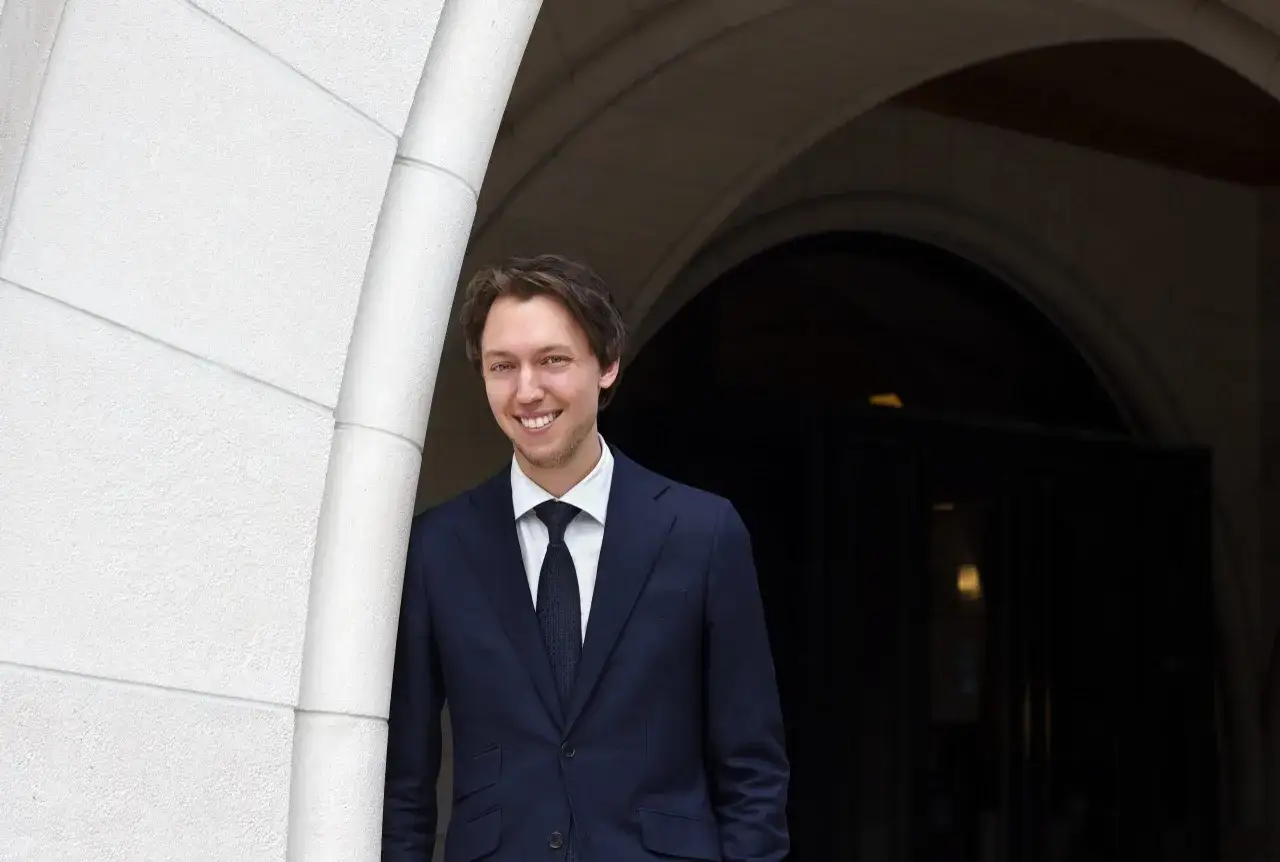 Ung man i mörk kostym ler vid en stenbåge. Han har precis avslutat sin advokatutbildning och ser fram emot framtiden.