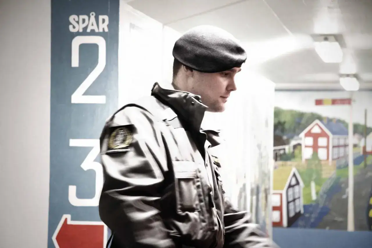 Man i uniform med basker, på väg till sin skyddsvakt utbildning. Skylt med