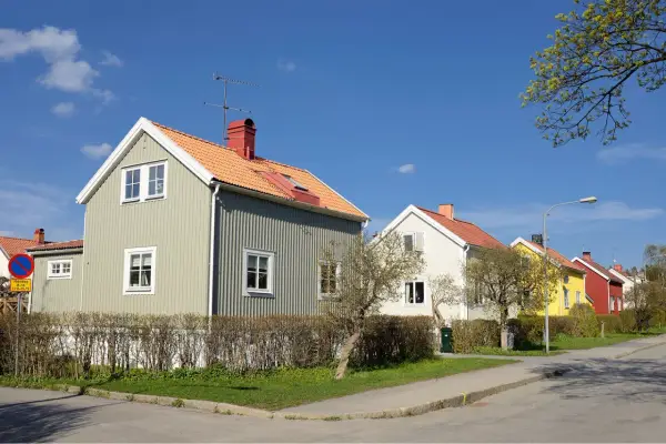 Rad av charmiga trähus i olika färger, med orange tak och gröna fasader. En dröm om ett hem med rimlig belåningsgrad.